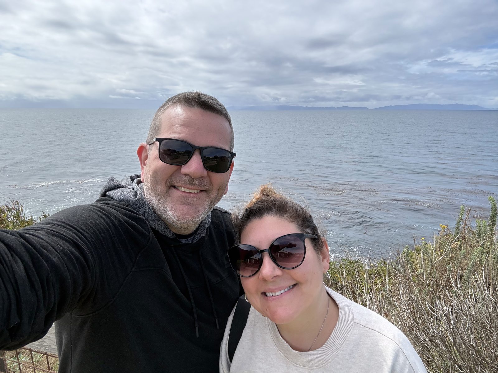 Bill and Carrolyn, in sunglasses, smile in a selfie on the Terranea bluff with the Pacific Ocean behind them.