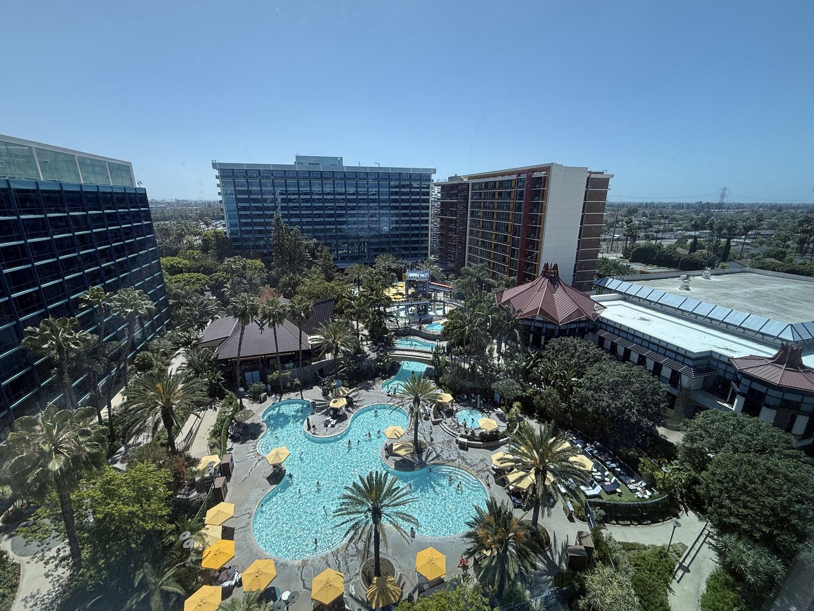 The Disneyland Hotel pool complex, with palm trees, cabanas and yellow umbrellas, seen from a guest room high above on a sunny day.